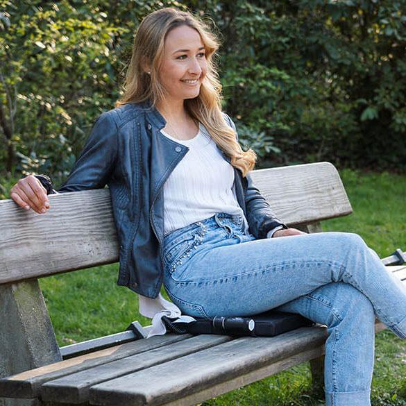 Eine Dame sitzt auf ihrem Weihnachtsgeschenk: Ein heatmyseat Heizkissen in der Farbe Schwarz. Das mobile Heizkissen nimm sie nun jeden Tag in den Park in der Mittagspause mit.